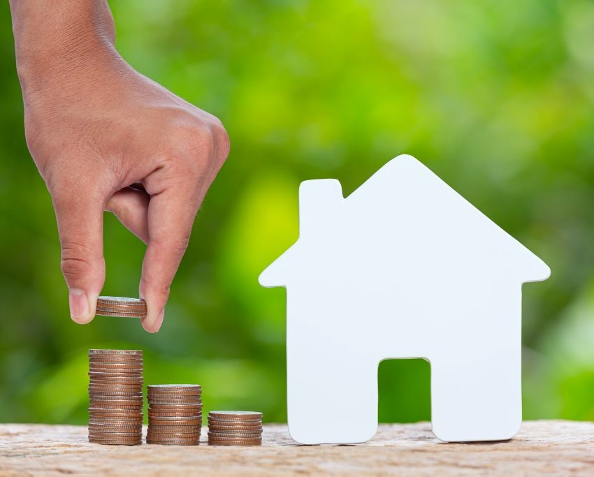 Wit houten huisje met daarnaast 3 stapeltjes met muntjes en een hand