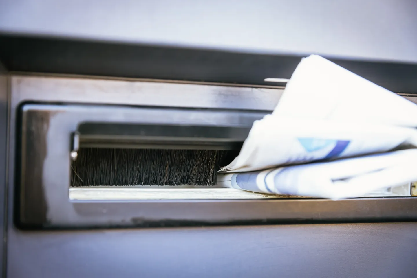 Brievenbus in deur met daarin brievenbusborstel en een krant die uitsteekt